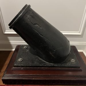 Antique cannon display in corner on wooden base.